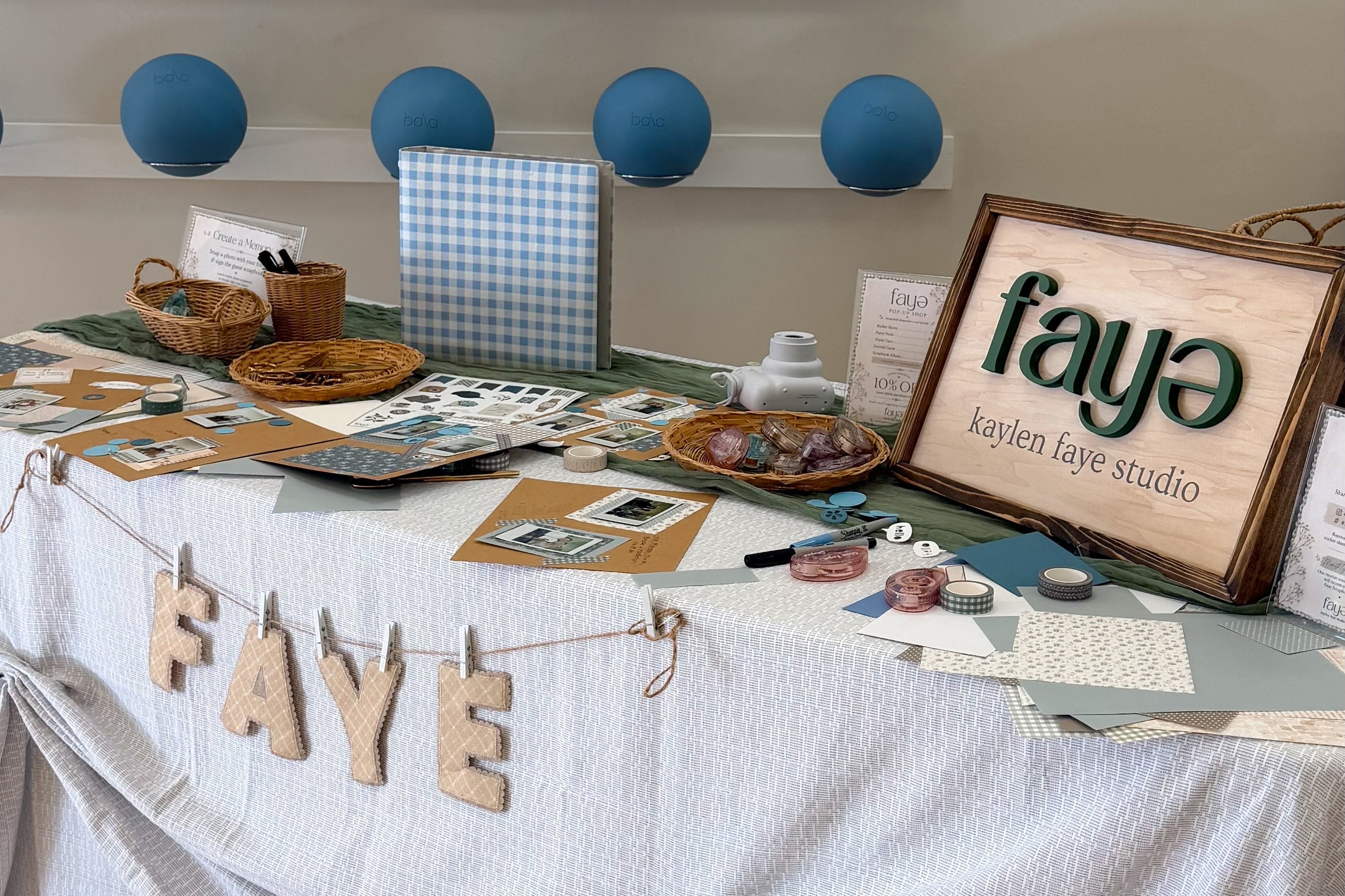 Table with 'FAYE' branding, decorative blue balls, and a framed picture on a light background.