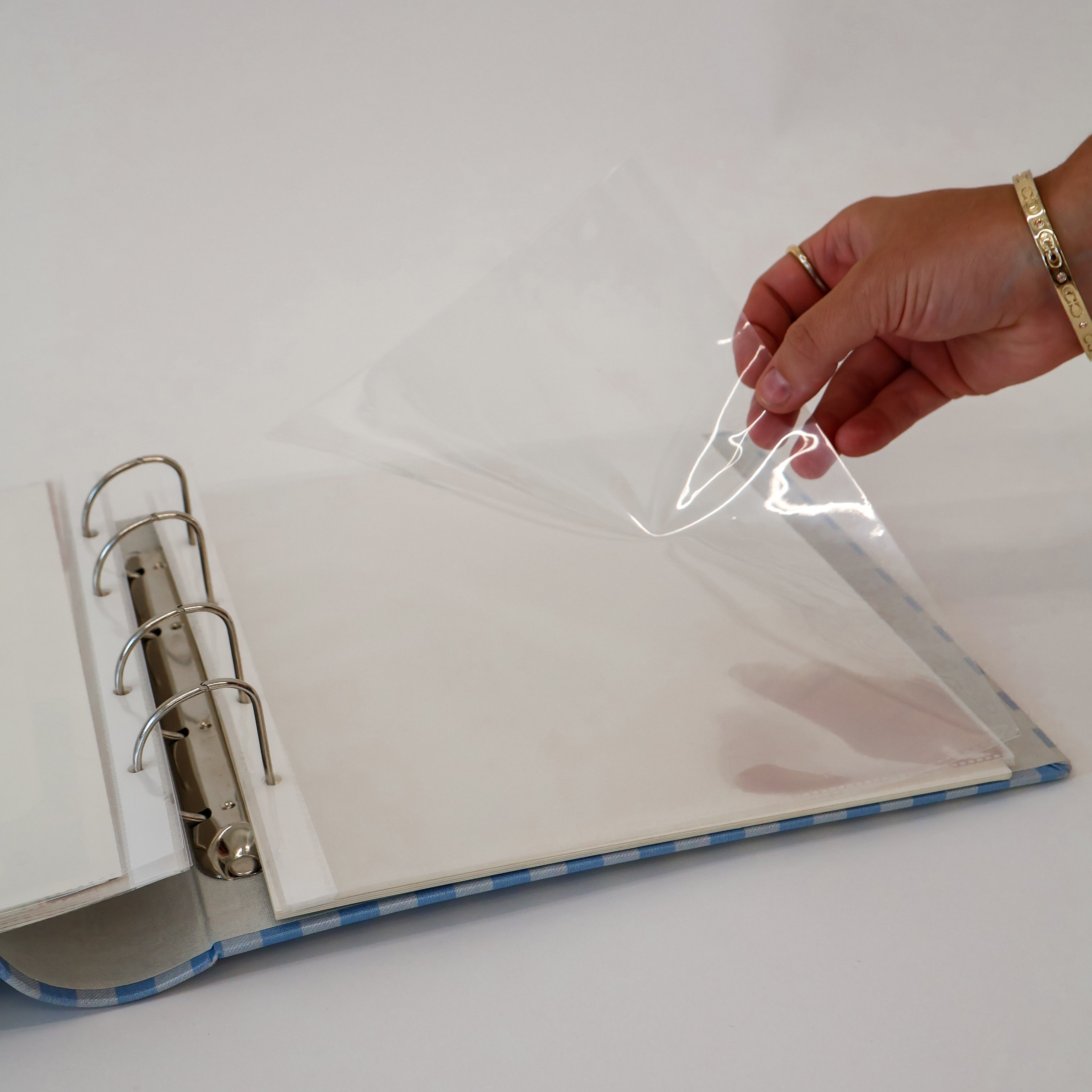 Hand holding a clear plastic page protectors over an open scrapbook with a white background