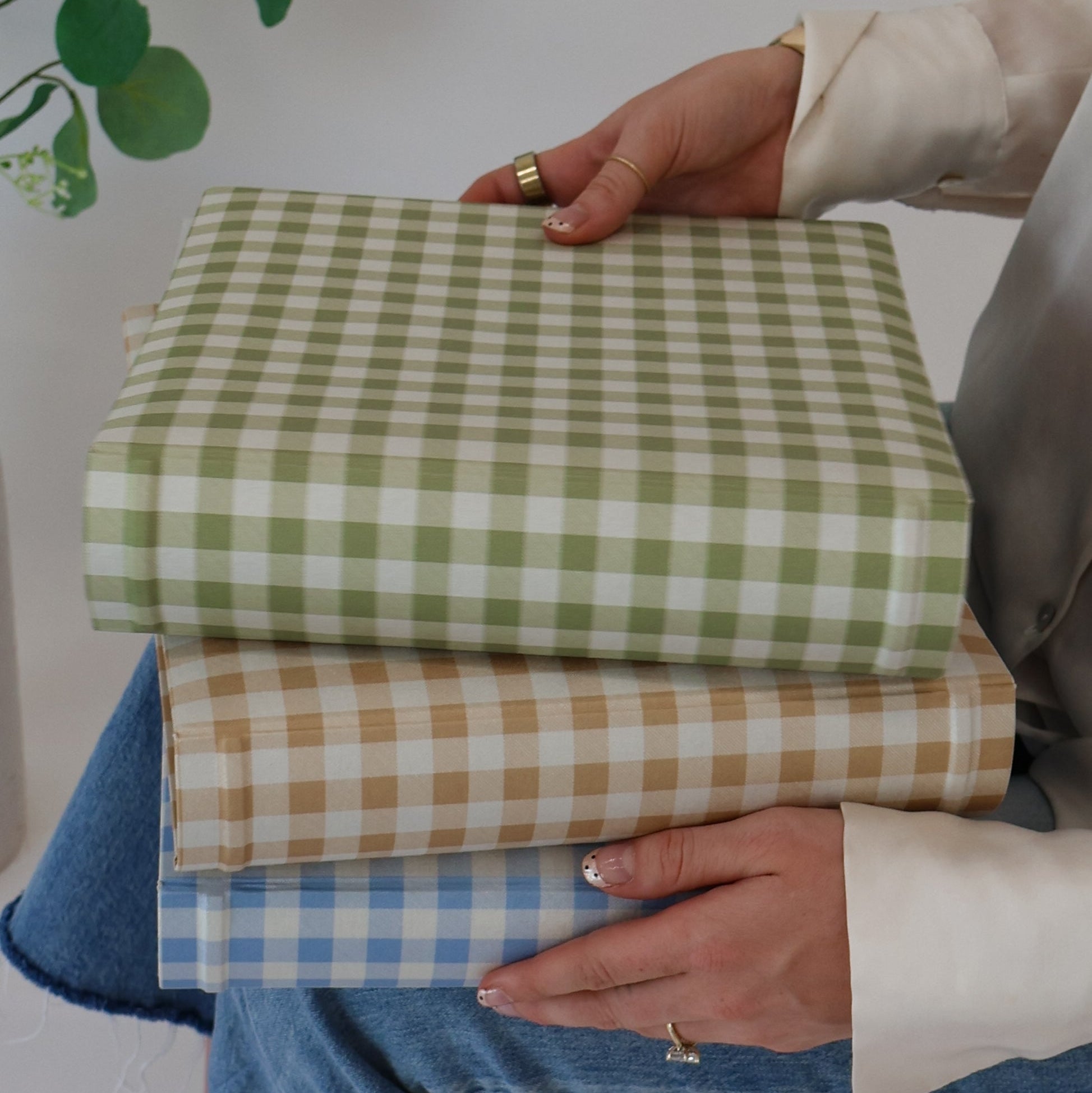 Person holding a stack of green, beige, and blue checkered scrapbook albums against a neutral background.
