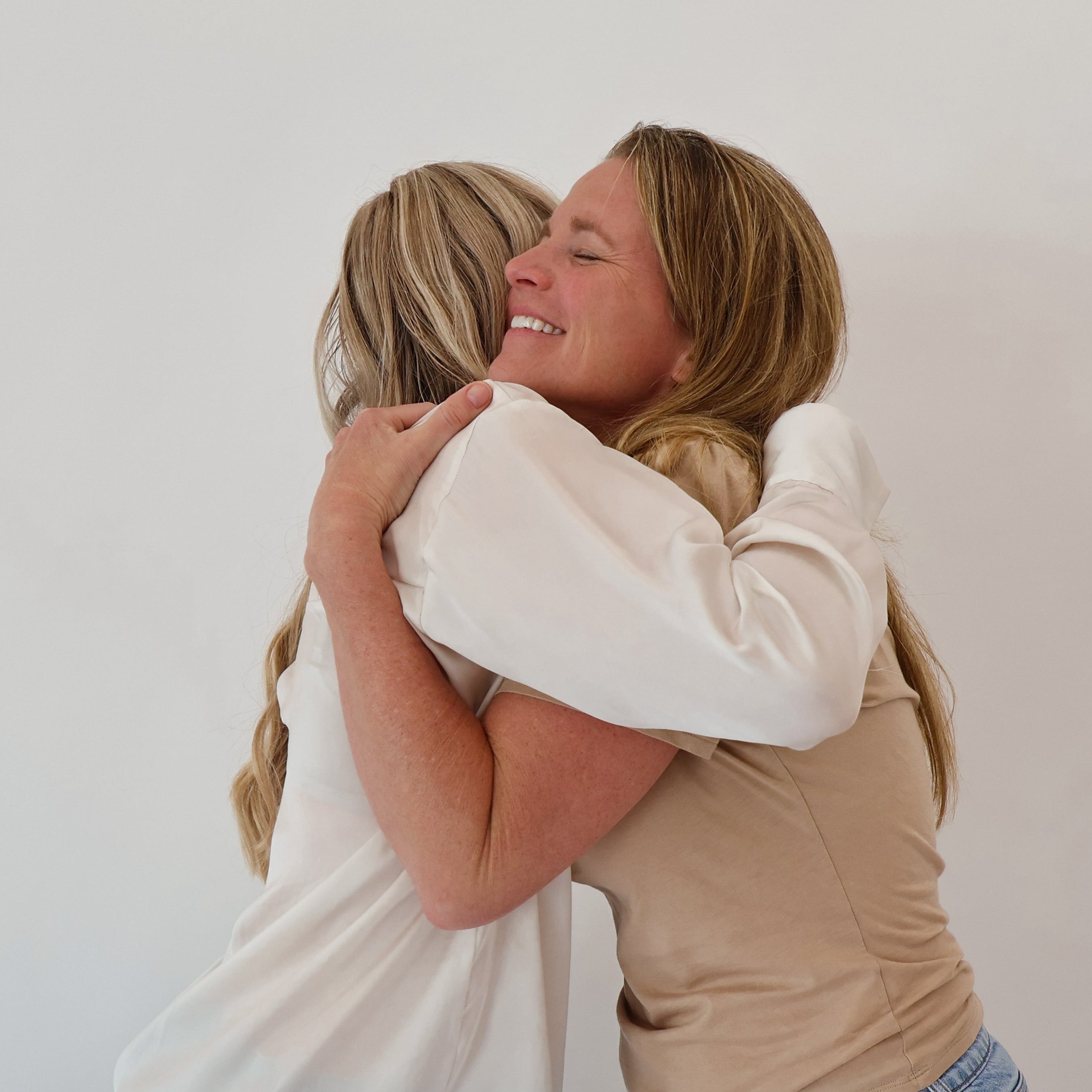 Two women hugging each other against a plain white wall.
