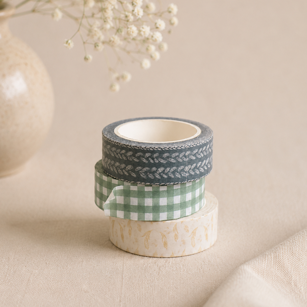 Set of washi tape rolls with decorative patterns on a beige surface with a vase and flowers in the background.