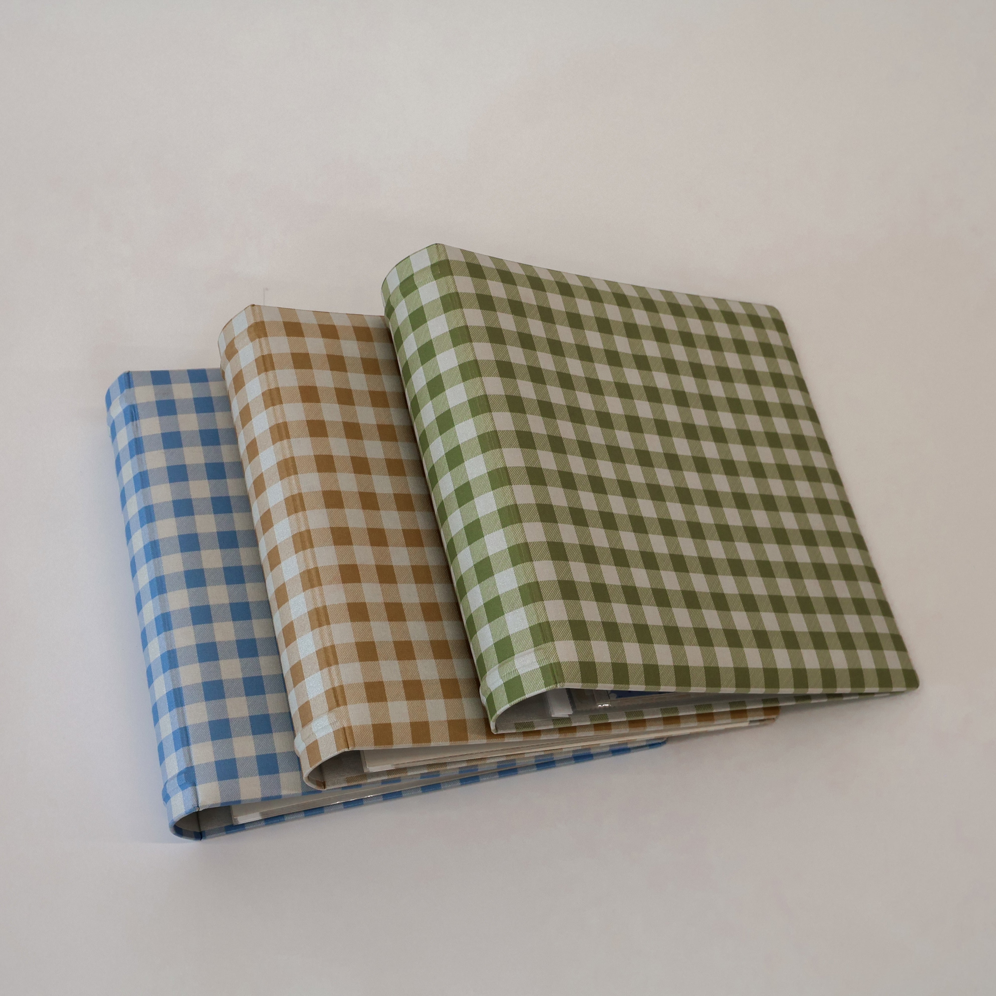 Three scrapbooks in blue, tan, and green checkered patterns on a white background.