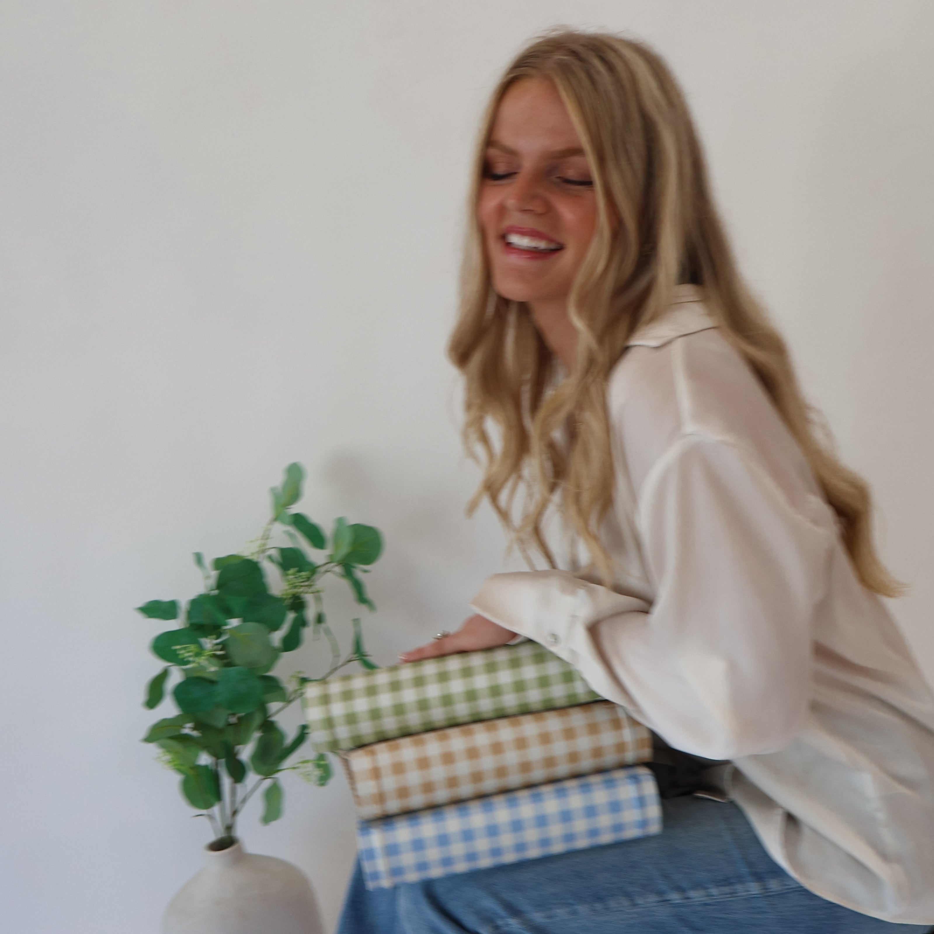 Woman sitting on a stool with a stack of colorful checkered scrapbook albums, smiling.